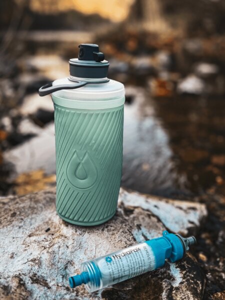 Skladacia fľaša Flux™ HydraPak<sup>&reg;</sup> s nasadeným filtrom na vodu HydraPak<sup>&reg;</sup> (28 mm) položená na kameni pri potoku. Foto: Rigad
