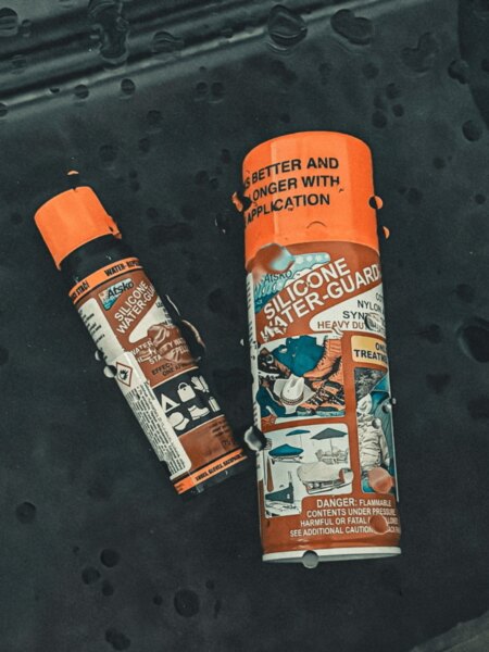 Impregnačné spreje Atsko Silicone Water-Guard položené na tmavej tkanine s kvapkami vody.