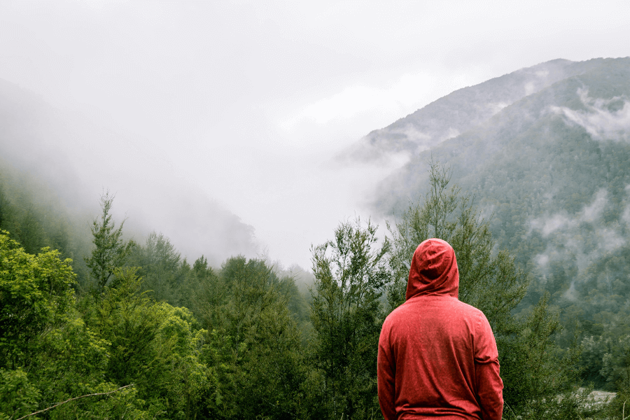 muž v červenej mikine stojí na horách v daždi