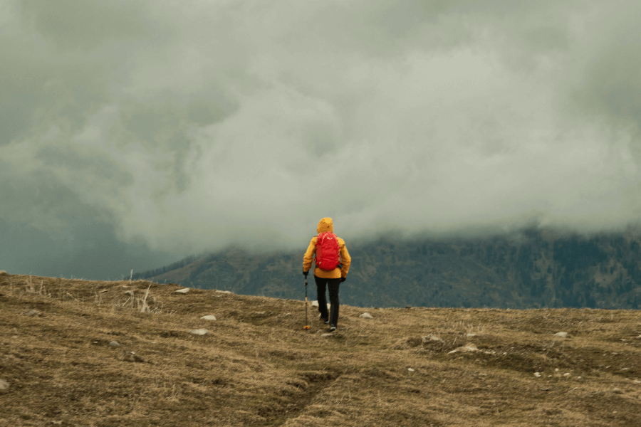 Muž v žltej bunde trekuje v horách v daždi