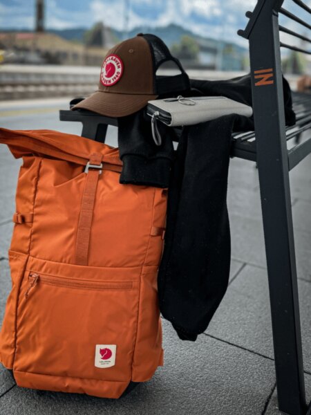 Oranžový batoh Fjällräven High Coast Foldsack 24 opretý o lavičku